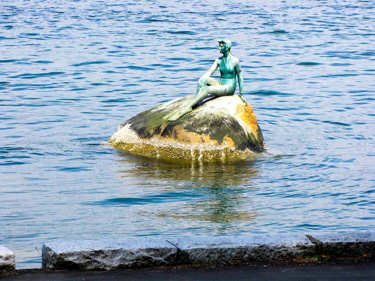 Bronze sculpture of a girl in a wetsuit sitting on a rock in the water