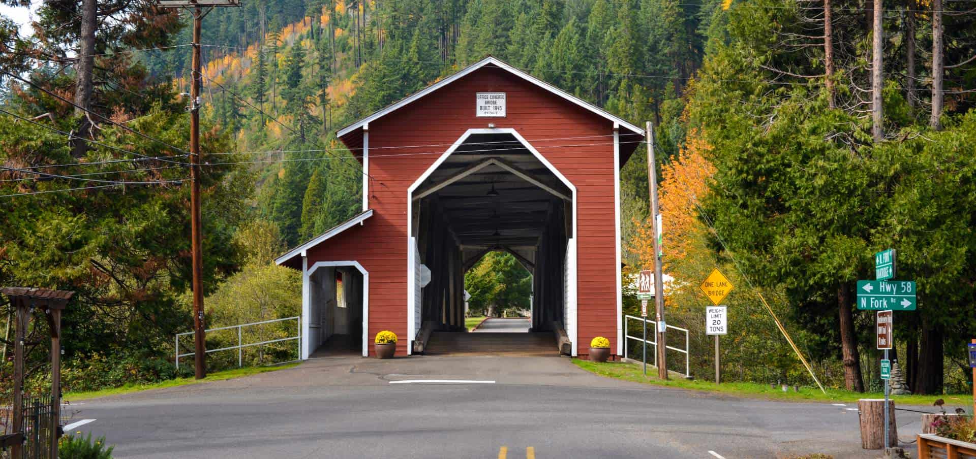 Red Office Covered Bridge in Westfir Oregon surrounded by green forest and mountain scenery