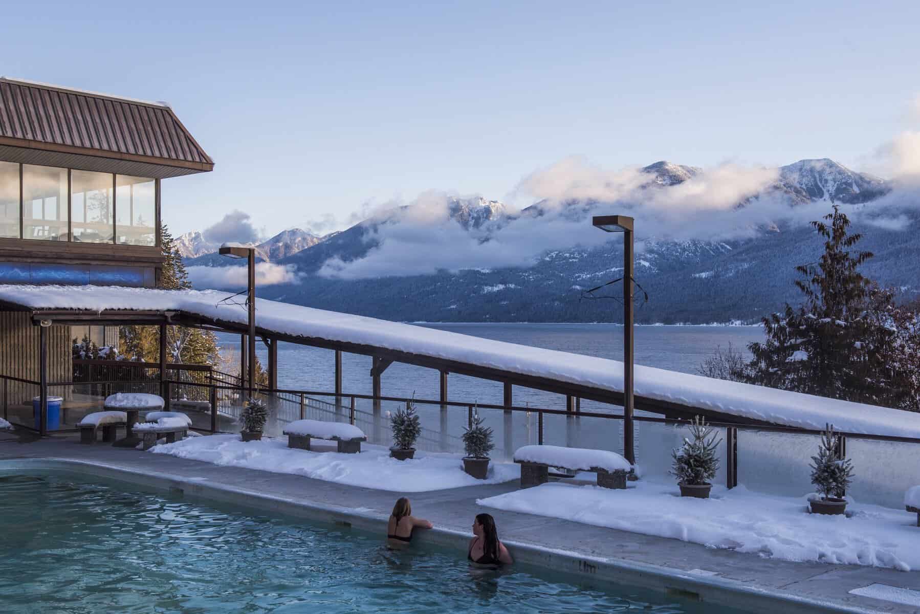 Visitors relaxing in the steaming outdoor mineral pool at Ainsworth Hot Springs during winter overlooking Kootenay Lake and snowy mountains