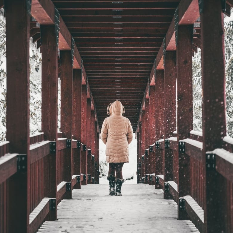 Person walking through a snow-covered red wooden bridge on the Kaslo River Trail in winter