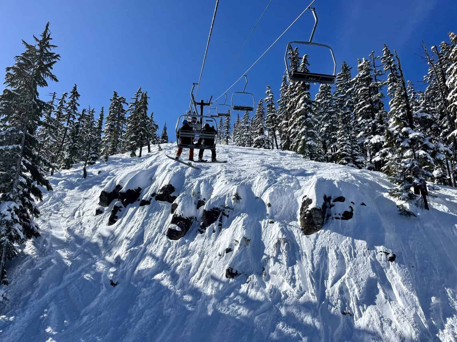 Chairlift carrying skiers above snow-covered slopes and evergreen forest at Willamette Pass Oregon